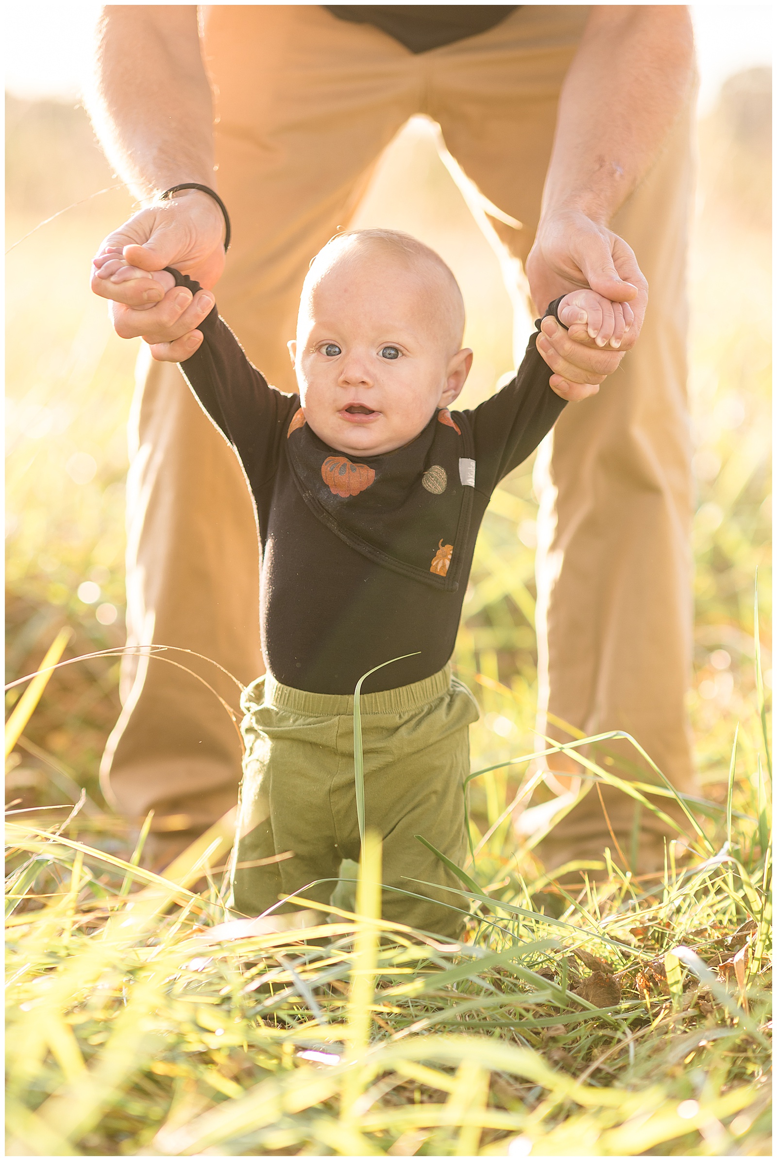 Rebecca Rice Photography captures baby boy in a field in Richmond, VA as he stands in the grass holding his dads hands.