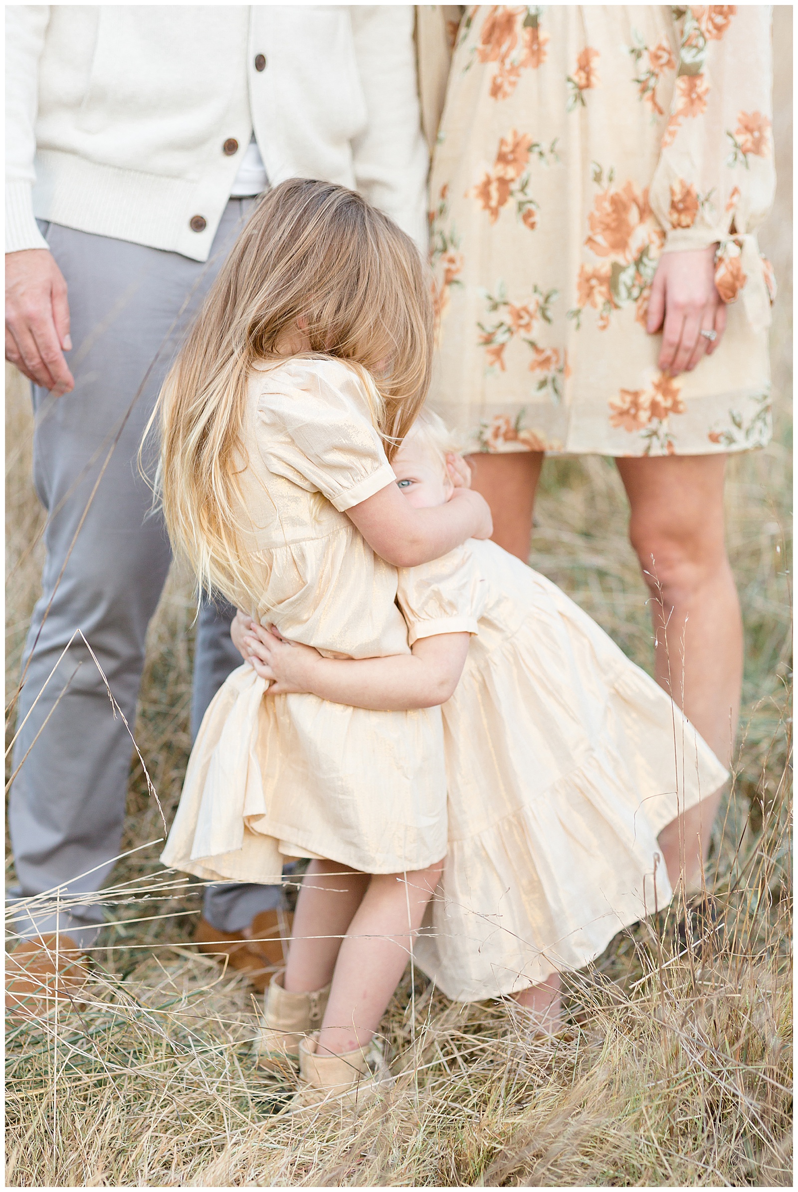 Two young sisters share a big hug as they hold each tightly wearing matching yellow/cream dresses during their family session in Nashville with Rebecca Rice Photography.