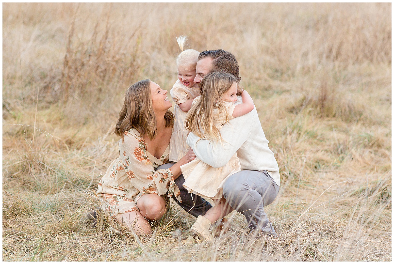 Nashville family photographer, Rebecca Rice, captures family of 4 in a Nashville field for her Behind the Lens membership.  Mom and Dad squat low as they share a big family hug and smile and laugh together!