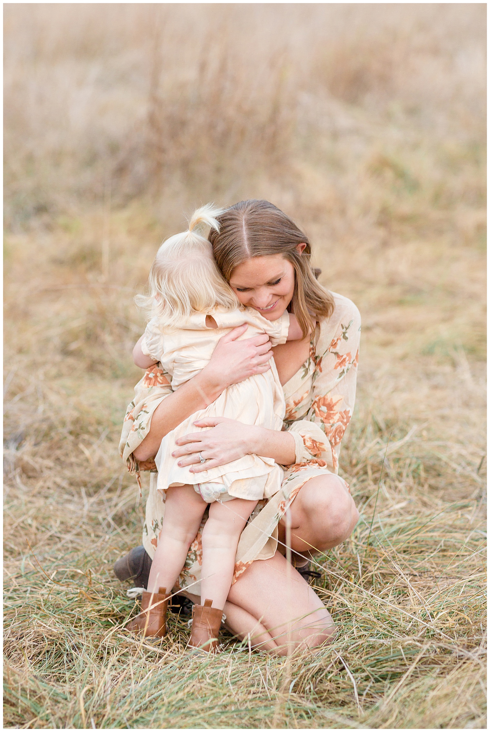 Mom bends down with her cream floral dress and hugs her toddler daughter tightly during their Nashville family session with Rebecca Rice.