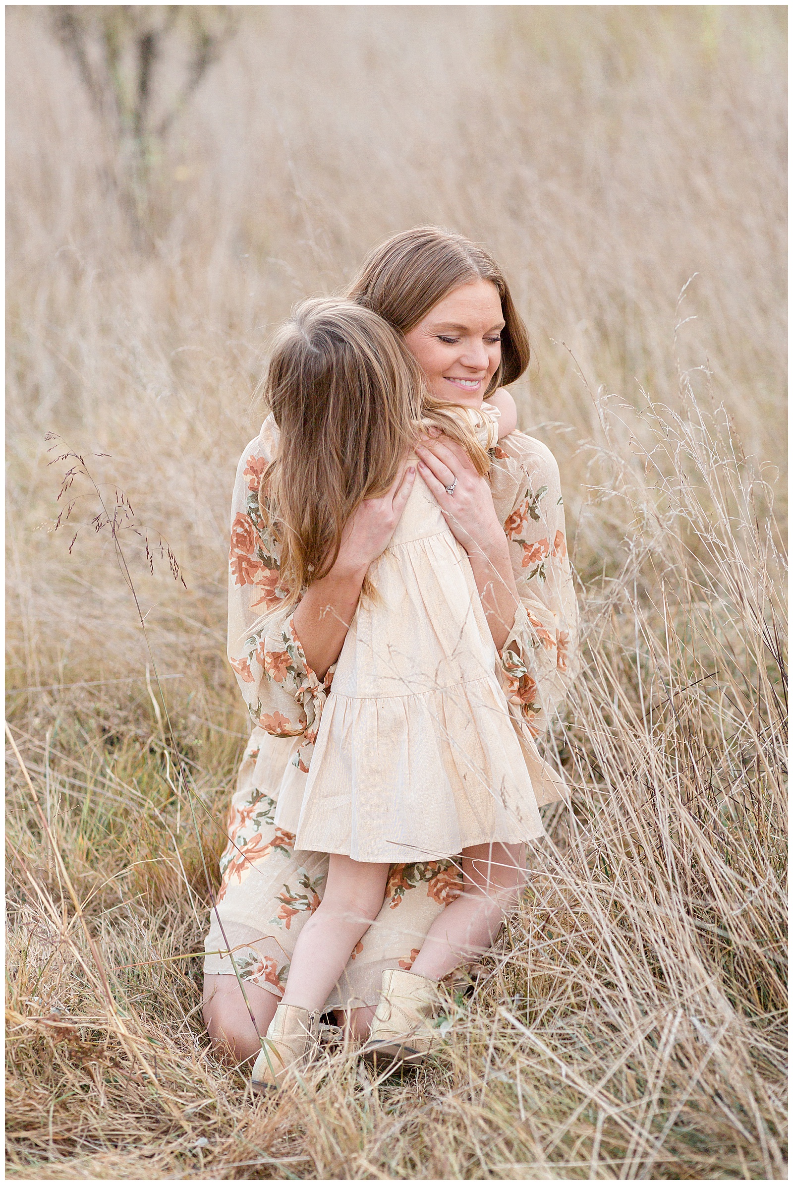 Mom and young daughter share a big hug together in a field in Nashville as they wear cream colored dresses.
