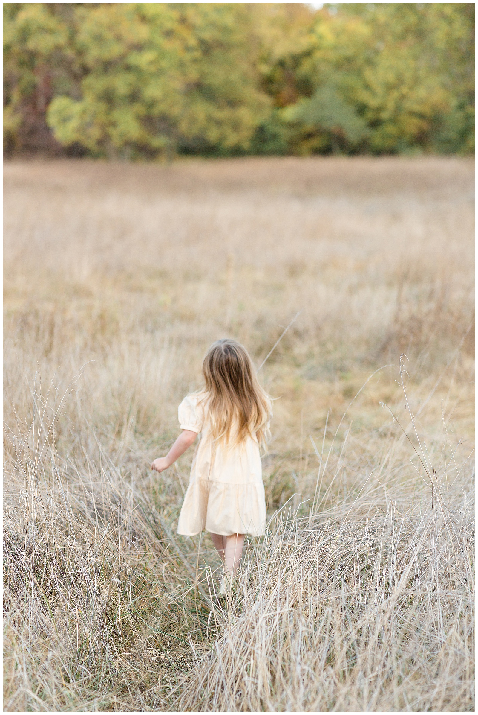 Little girl wears a cream colored dress with her hair down as she runs away from the camera through a field in Nashville!  Click to see more on the blog of this Nashville family session.