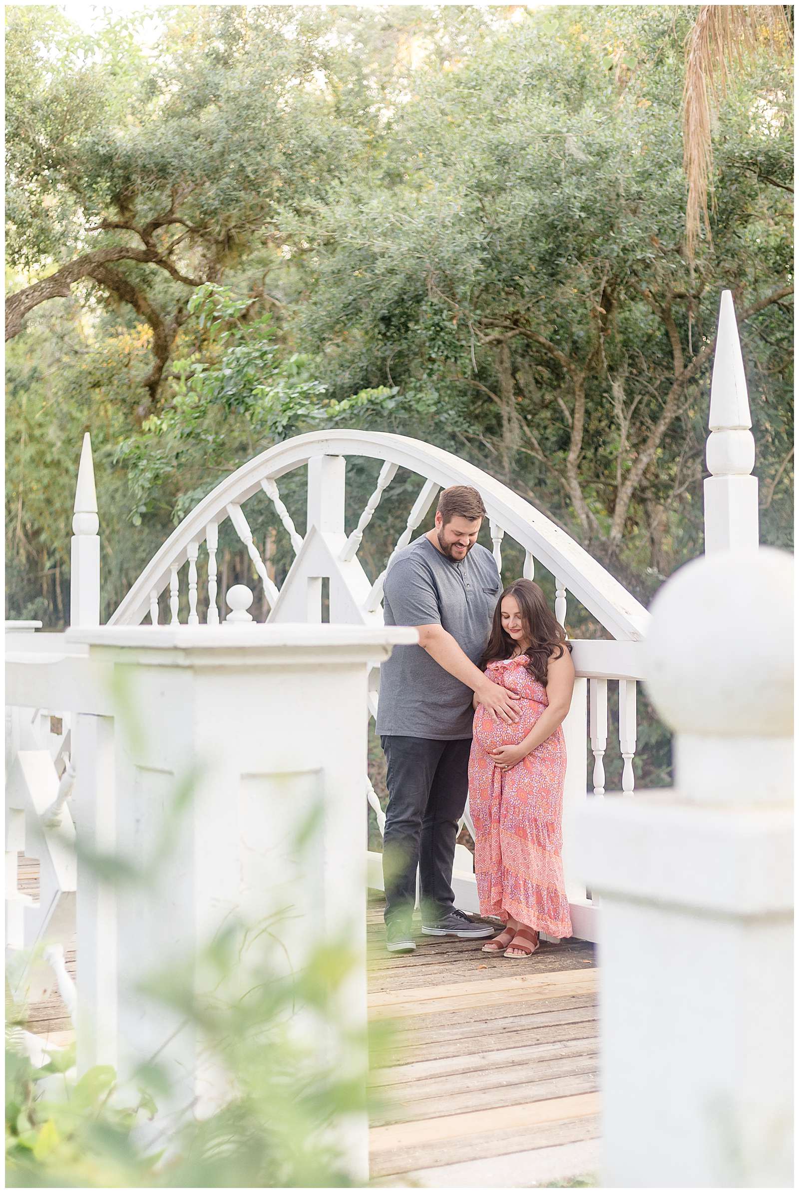 Tall husband looks down as his pregnant wife's belly and puts his hand on it while she holds from underneath.  They stand on a bridge surrounded by Florida moss trees during their Florida maternity session with Rebecca Rice Photography.  Click to see more from this session on the blog today!
-rebeccaricephoto.com
