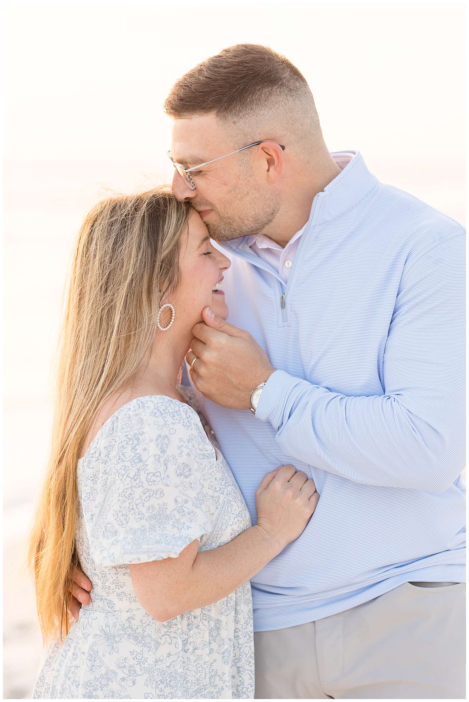Rosemary Beach family session features an image of a couple standing close together as she puts her hand on his belly and he pulls her in close and holds her chin while giving her a kiss on her forehead.  They coordinate in white, and light blue.  See more of this photography couple on the blog today! -rebeccaricephoto.com