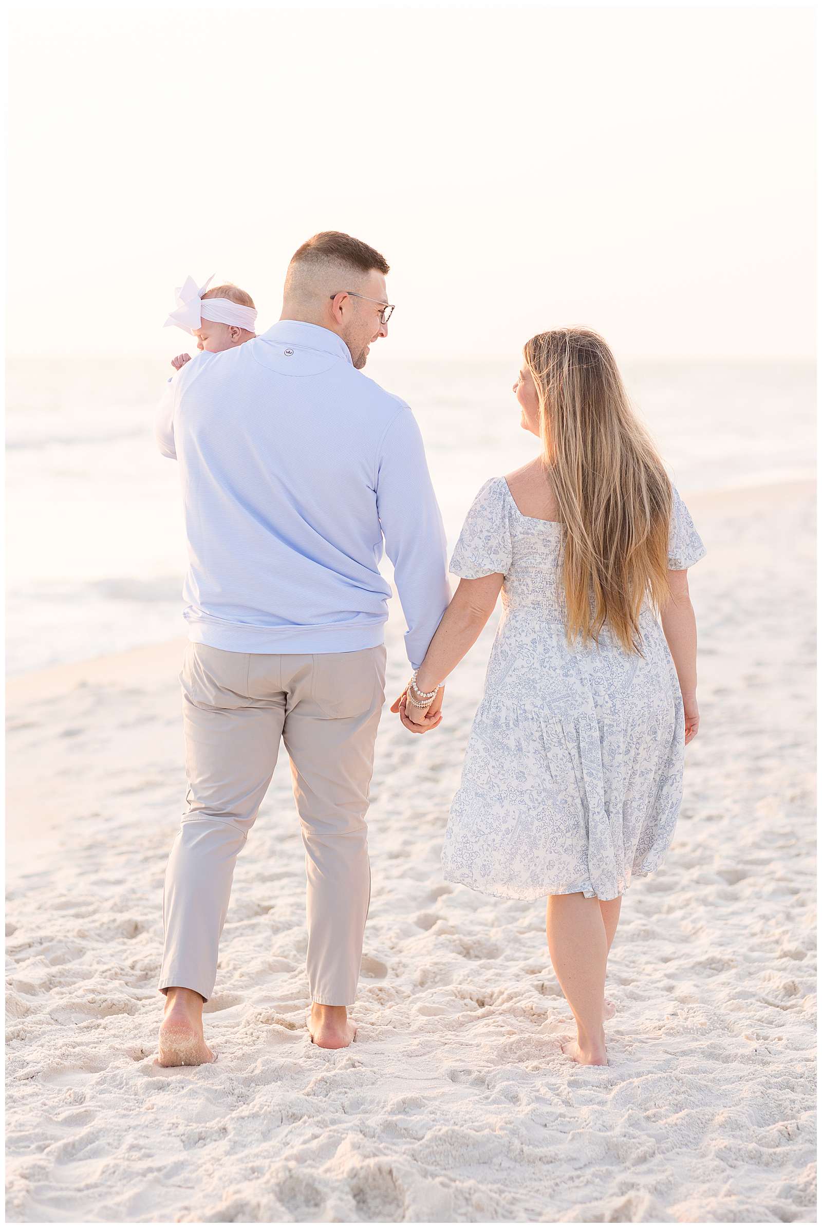 Family of 3, with new baby girl, shows image of couple holding hands and looking at each other as they walk the beach and Dad holds his baby girl up over his shoulder.  This sweet, Rosemary Beach family session is on the blog today! - rebeccaricephoto.com