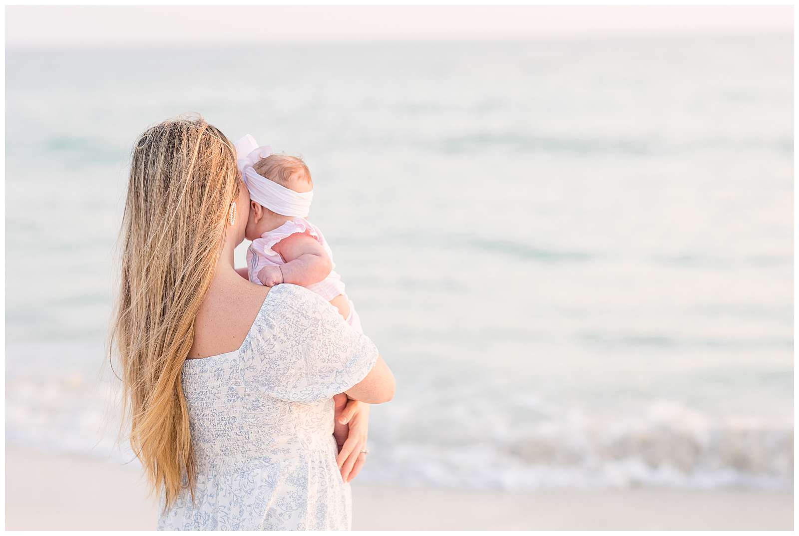 Sweet image taken by Rosemary Beach photographer, Rebecca Rice, captures the beach in the background and new mom, who holds her baby girl to her cheek, looking out at the beautiful beach at sunset.  Click to see more from this beach session on the blog! -rebeccaricephoto.com