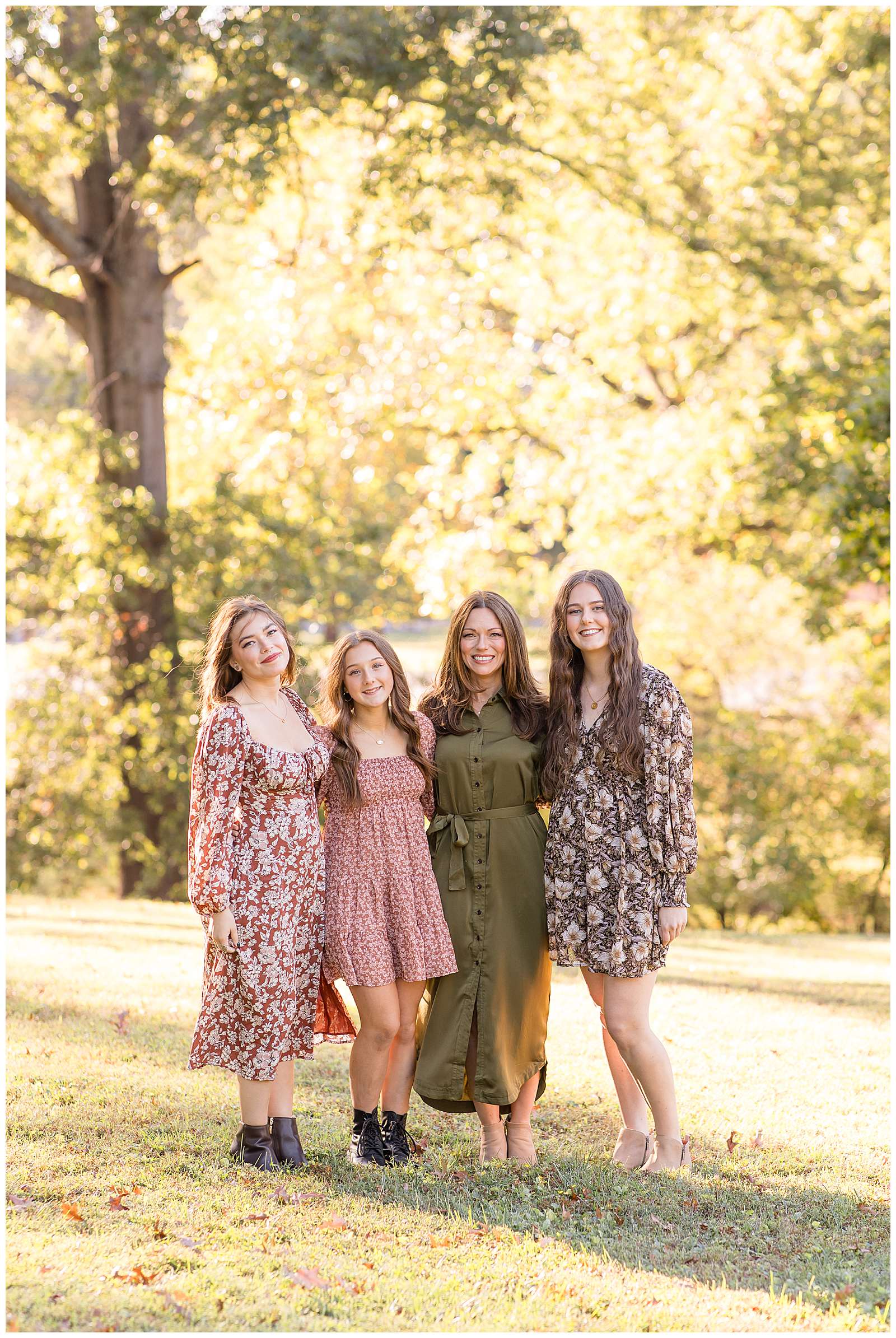 A mom wearing an olive, button-down dress stands with her daughter and her sons girlfriends during their fall, family photography session.  The girls wear long sleeve dresses and booties in fall floral prints.