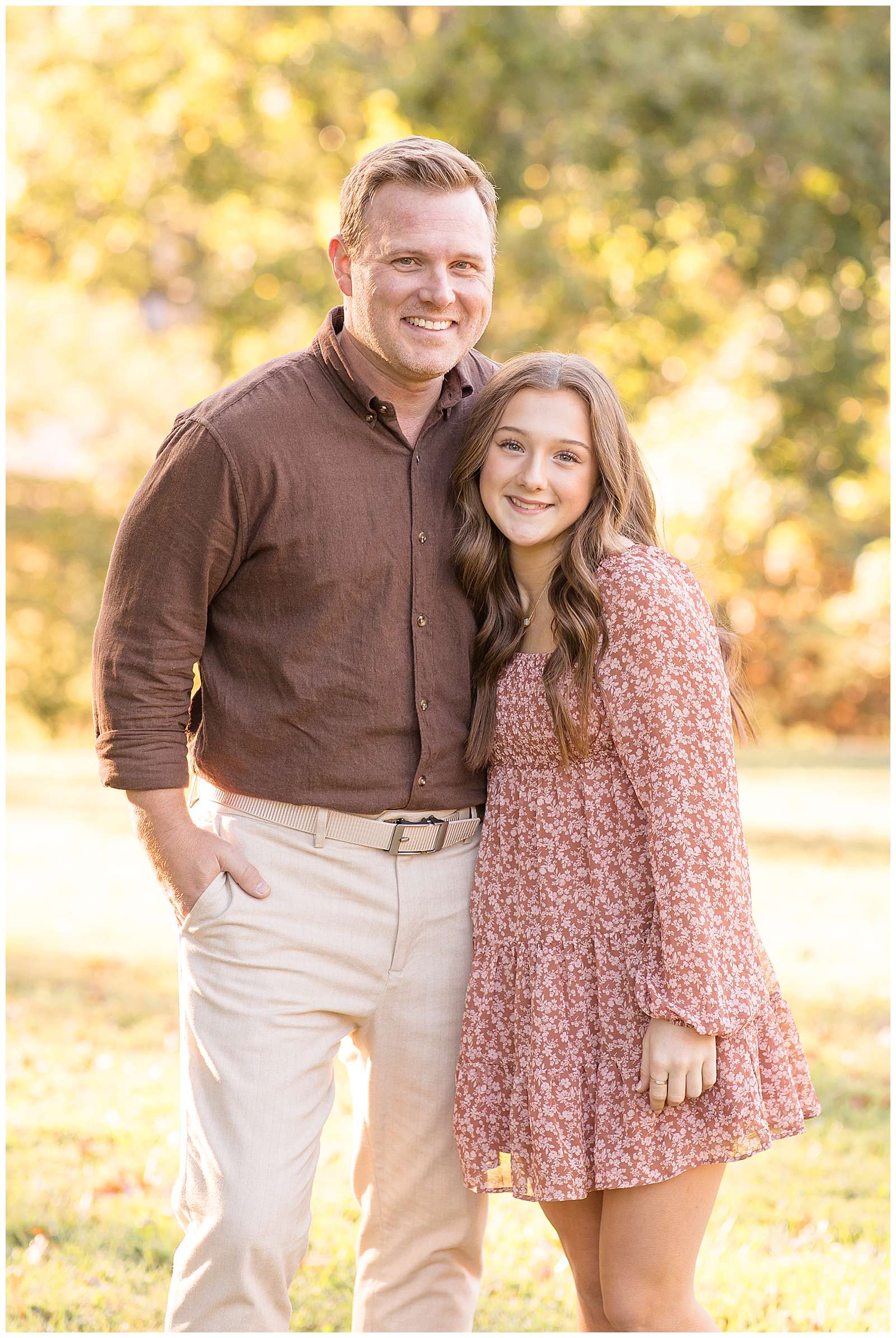 Family Photography Educator, Rebecca Rice captures an image of a Dad and his high school aged daughter during their fall family session.  Dad wears a brown, button down shirt and khaki pants and his daughter wears a dusty rose, long sleeve dress with small white flowers all over.