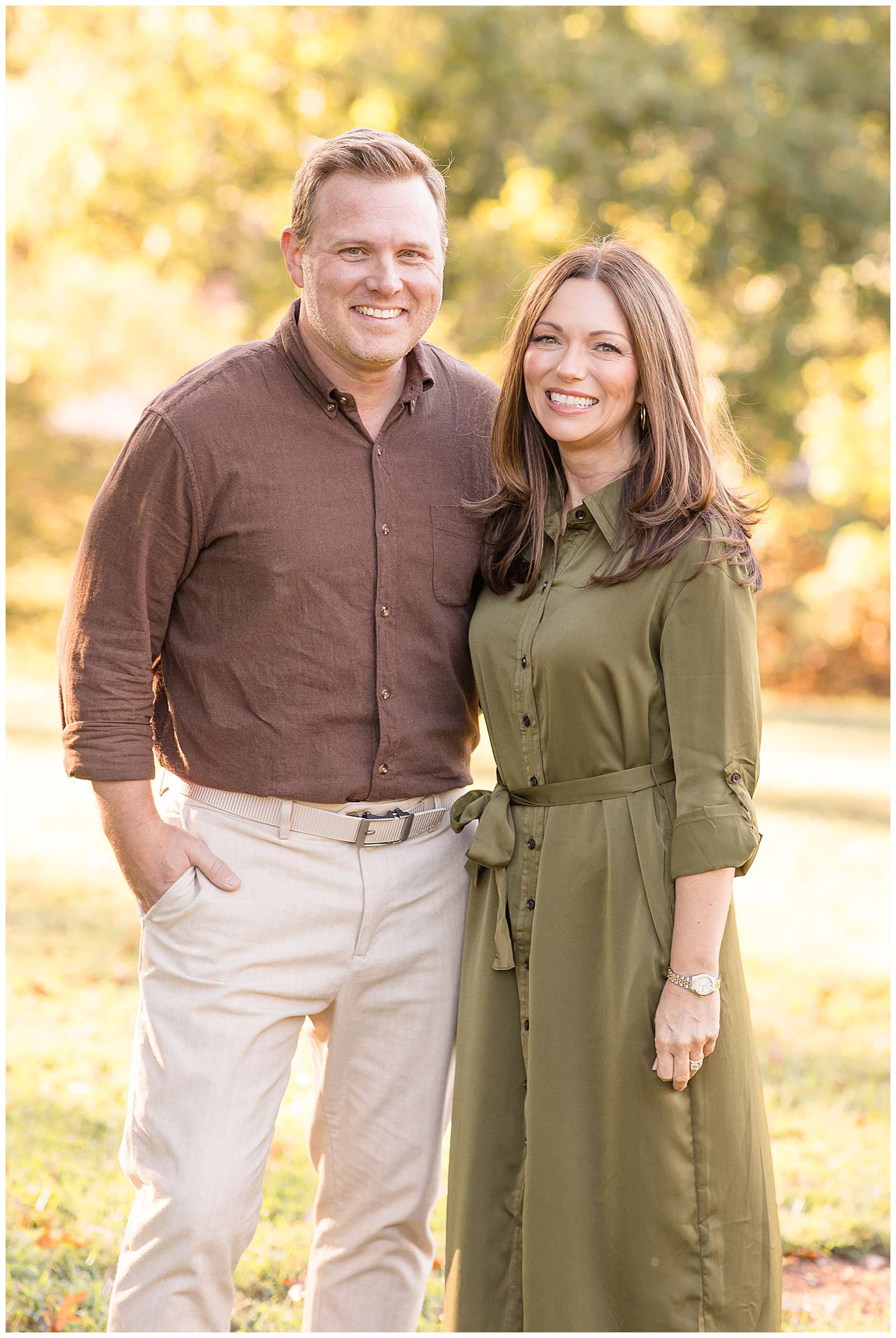 Rebecca Rice, family photography educator, takes a picture of parents with grown children by themselves during their fall family photography portraits.  Mom wears an olive green, button down dress and Dad wears khaki pants and a brown, long sleeve button down shirt.